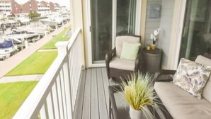 Ein Balkon mit Blick auf eine Marina, ein Sessel, ein kleiner Tisch mit einer Pflanze und eine Couch mit Kissen.