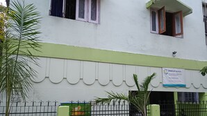 A building with a green and white facade, a sign for 'SWAROOP ASHRAY' indicating a homestay, and a fenced area with a sign for 'Banyly Fresh' offering fresh juices and salads. - Swaroop Ashray (Siliguri)