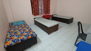 A room with two beds, a chair, and a window with curtains. - Swaroop Ashray (Siliguri)