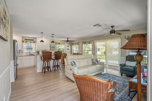 A spacious living area with a sofa, chairs, a dining table, and a kitchen in the background. - Ostego Charm: Brand new pool, porch, lush landscape—walk-able to the Beach! (Fort Myers Beach)