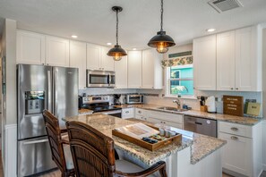 A modern kitchen with stainless steel appliances, a granite countertop, and a central island with seating. - Ostego Charm: Brand new pool, porch, lush landscape—walk-able to the Beach! (Fort Myers Beach)