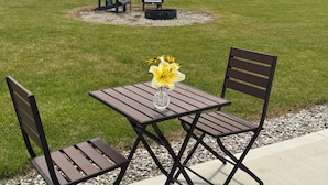An outdoor patio with a table and chairs, a vase with flowers, and a fire pit in the background. - The Sunset Dome- a private escape, with breathtaking sunsets, rooted in nature. (Guelph/Eramosa)