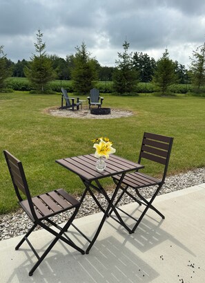 An outdoor patio with a table and chairs, a vase with flowers, and a fire pit in the background. - The Sunset Dome- a private escape, with breathtaking sunsets, rooted in nature. (Guelph/Eramosa)