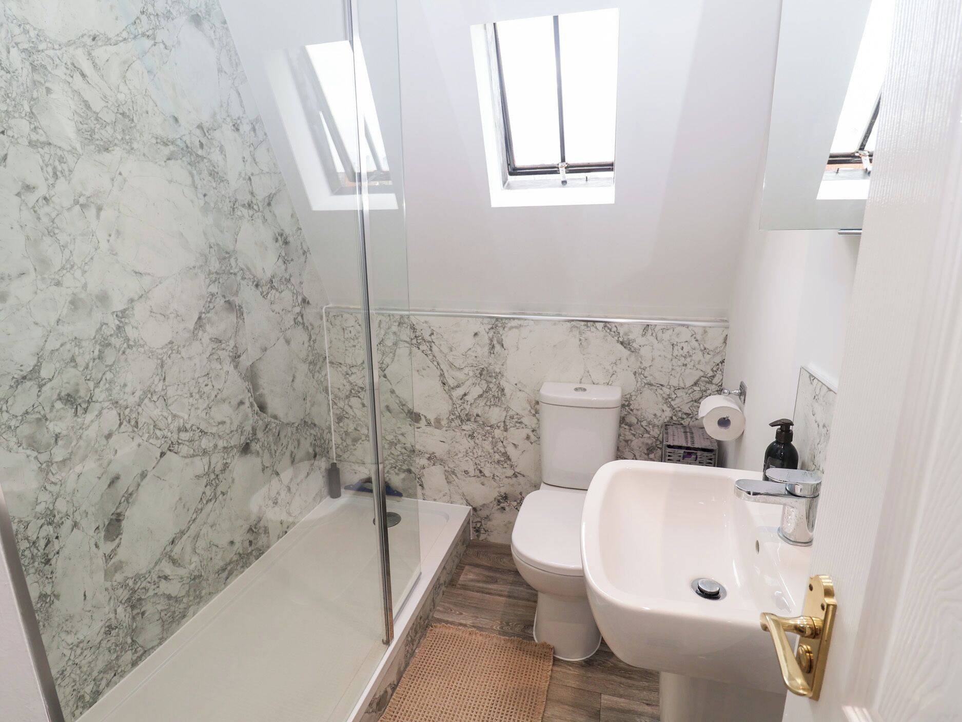 Une salle de bain avec un mur en marbre, une cabine de douche en verre, des toilettes, un lavabo et une fenêtre.