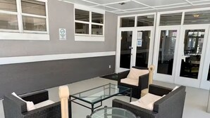 An outdoor seating area with wicker furniture and glass tables, a trash bin, and a door with a sign. - Condo Near Disney No Resort Fee Free Parking (Kissimmee)