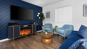 Un salon moderne avec un téléviseur à écran plat, une cheminée, des canapés bleus et une table basse.