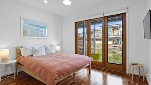Un dormitorio con cama, mesita de noche, lámpara, un cuadro y una puerta corrediza de vidrio que da a un espacio exterior.