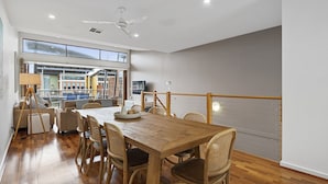 Un comedor con mesa y sillas de madera, ventilador de techo y ventanas amplias con vistas a una terraza.