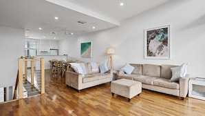 Amplia sala de estar con piso de madera, un conjunto de sof á color beige, un comedor con mesa y sillas, y una cocina al fondo.