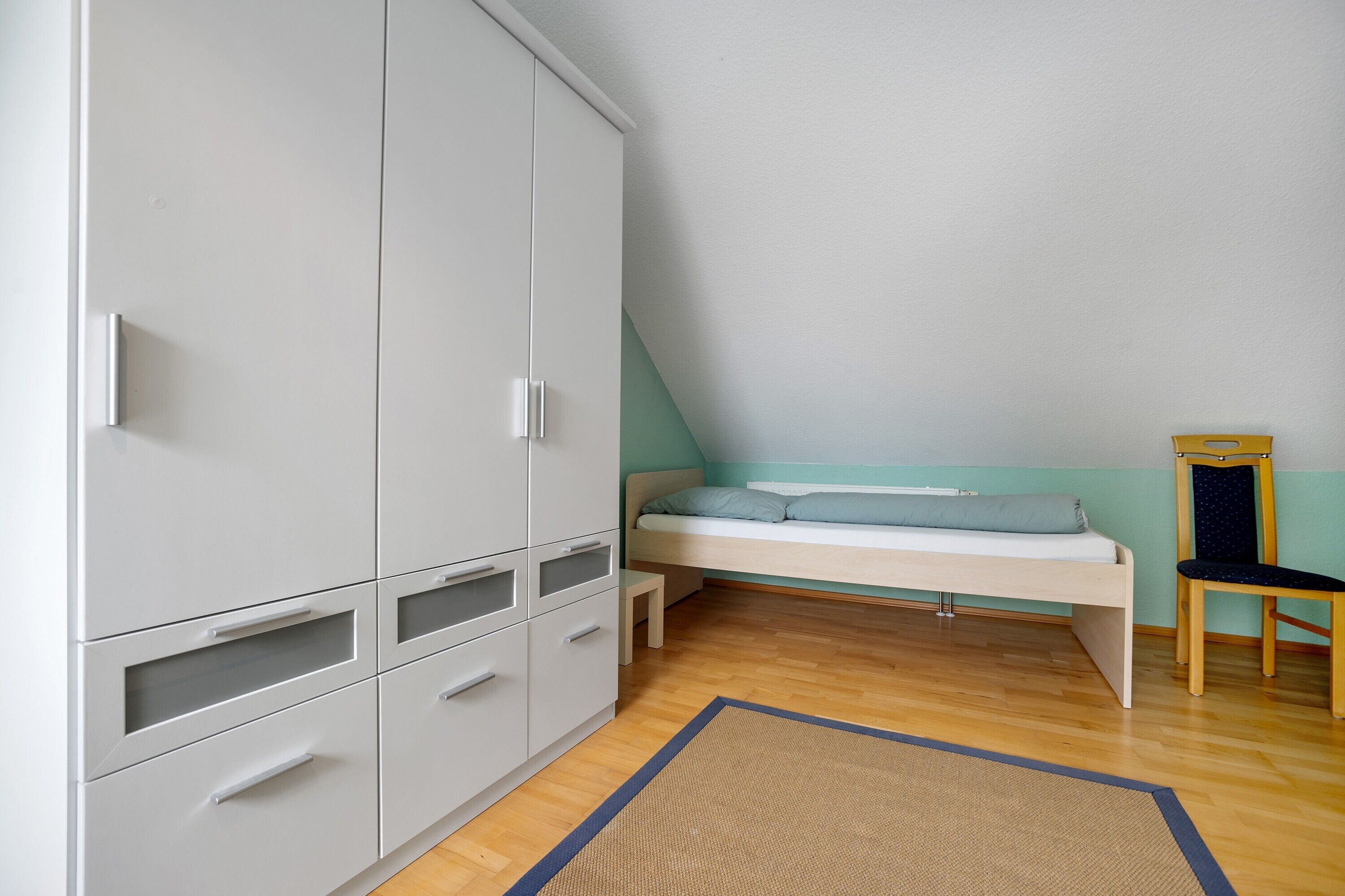 Un dormitorio con cama, armario, silla y una pequeña mesa.