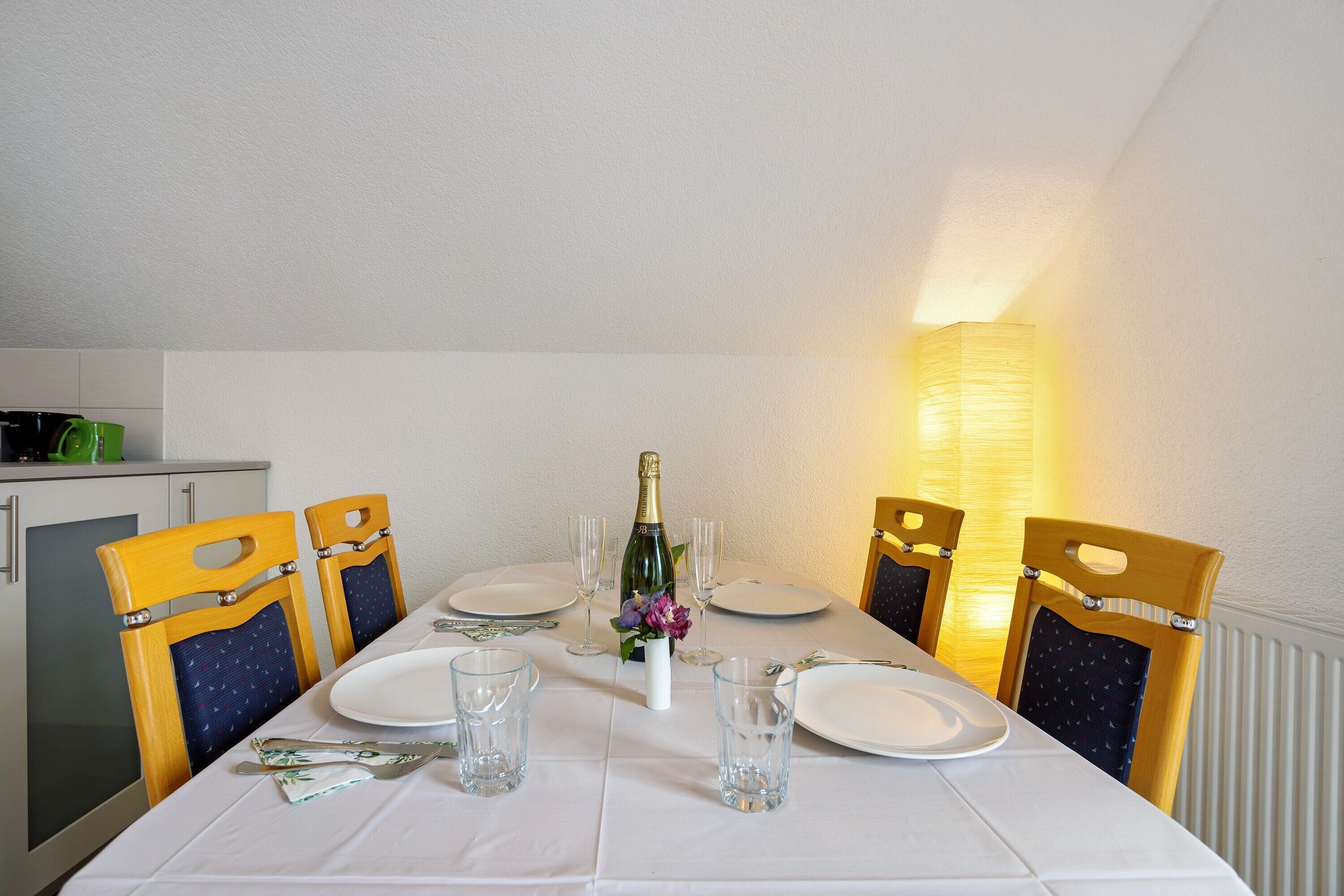 A dining table set for six with chairs, a bottle of champagne, and a vase of flowers.