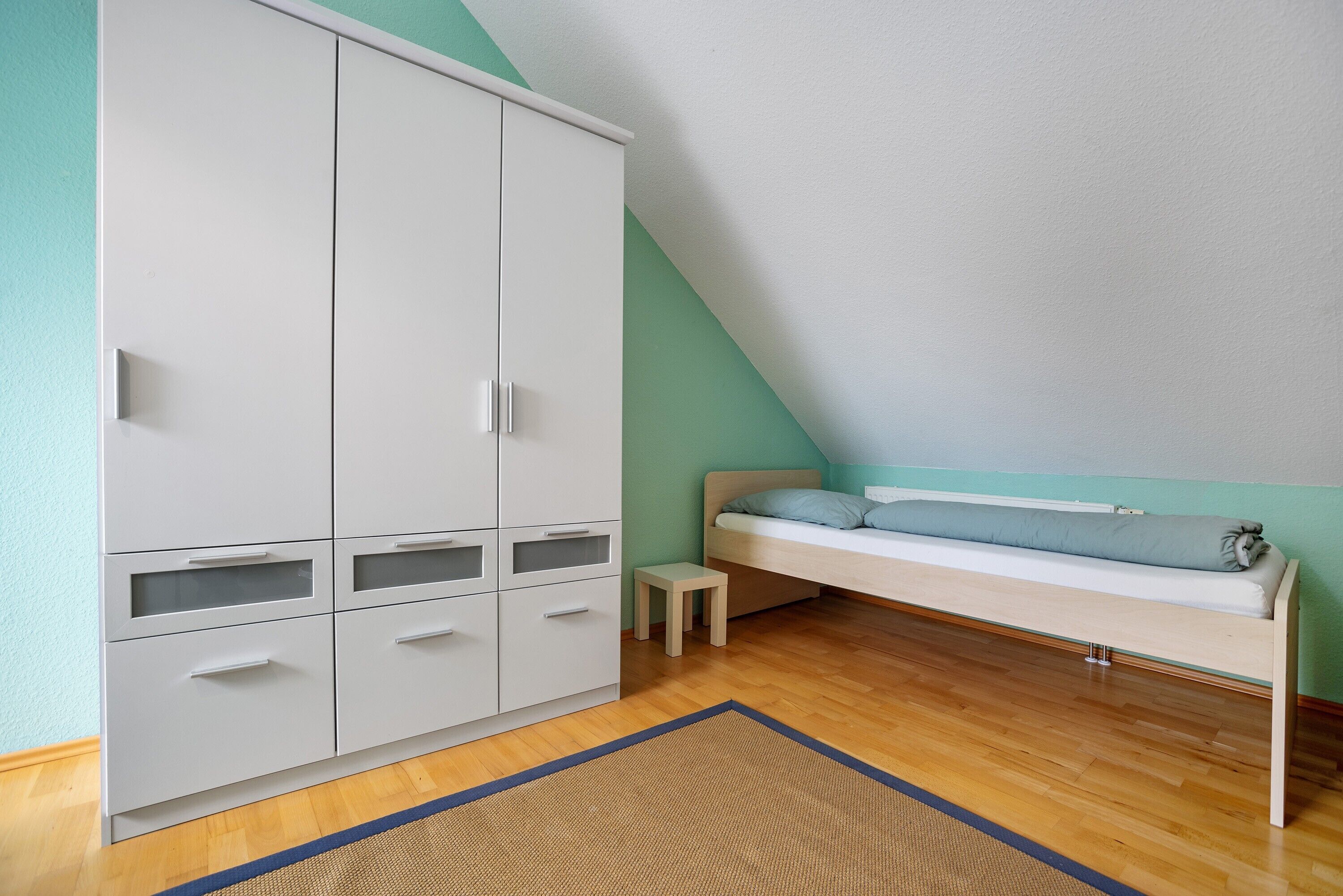 A room with a bunk bed, a wardrobe, and a small stool.