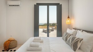 A bedroom with a bed, pillows, a bedside lamp, an air conditioning unit, and a view of the outdoors. - Near Naousa |3BR Villa| Private Pool |Villa Candia (Paros)