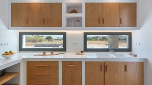 A modern kitchen with wooden cabinets, a large window, and a built-in sink. - Near Naousa |3BR Villa| Private Pool |Villa Candia (Paros)