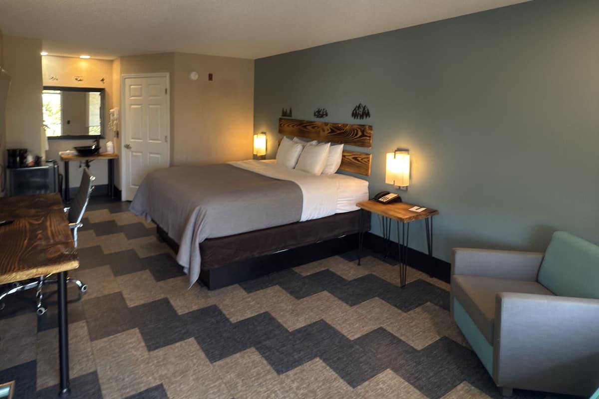 Una habitación de hotel con cama, mesita de noche, silla y una pequeña zona de kitchenette.