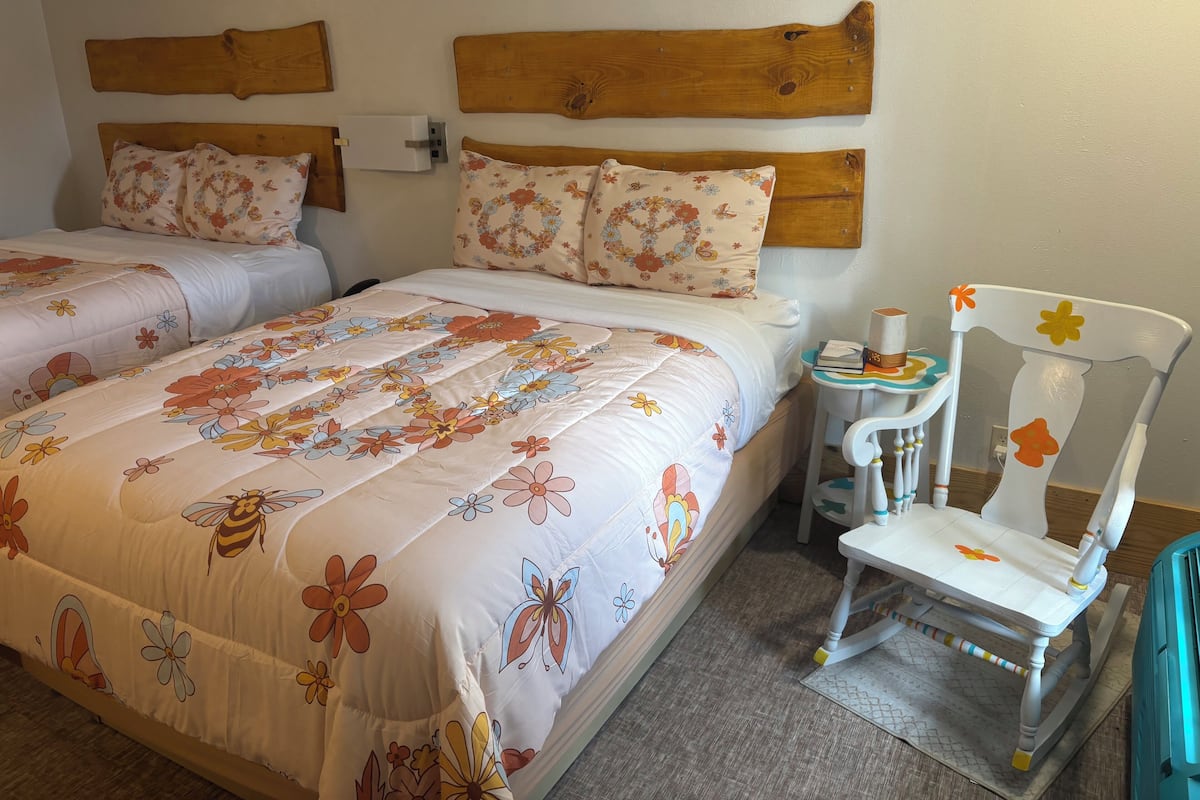 Una cama doble con ropa de cama floral, un cabecero de madera y una mesita de noche pequeña con una lámpara.