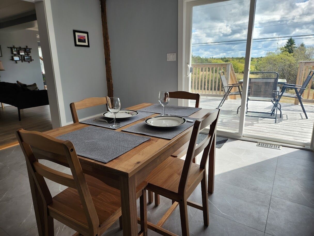 A dining area with a wooden table set for two, a glass door leading to an outdoor patio, and a view of the outdoors.