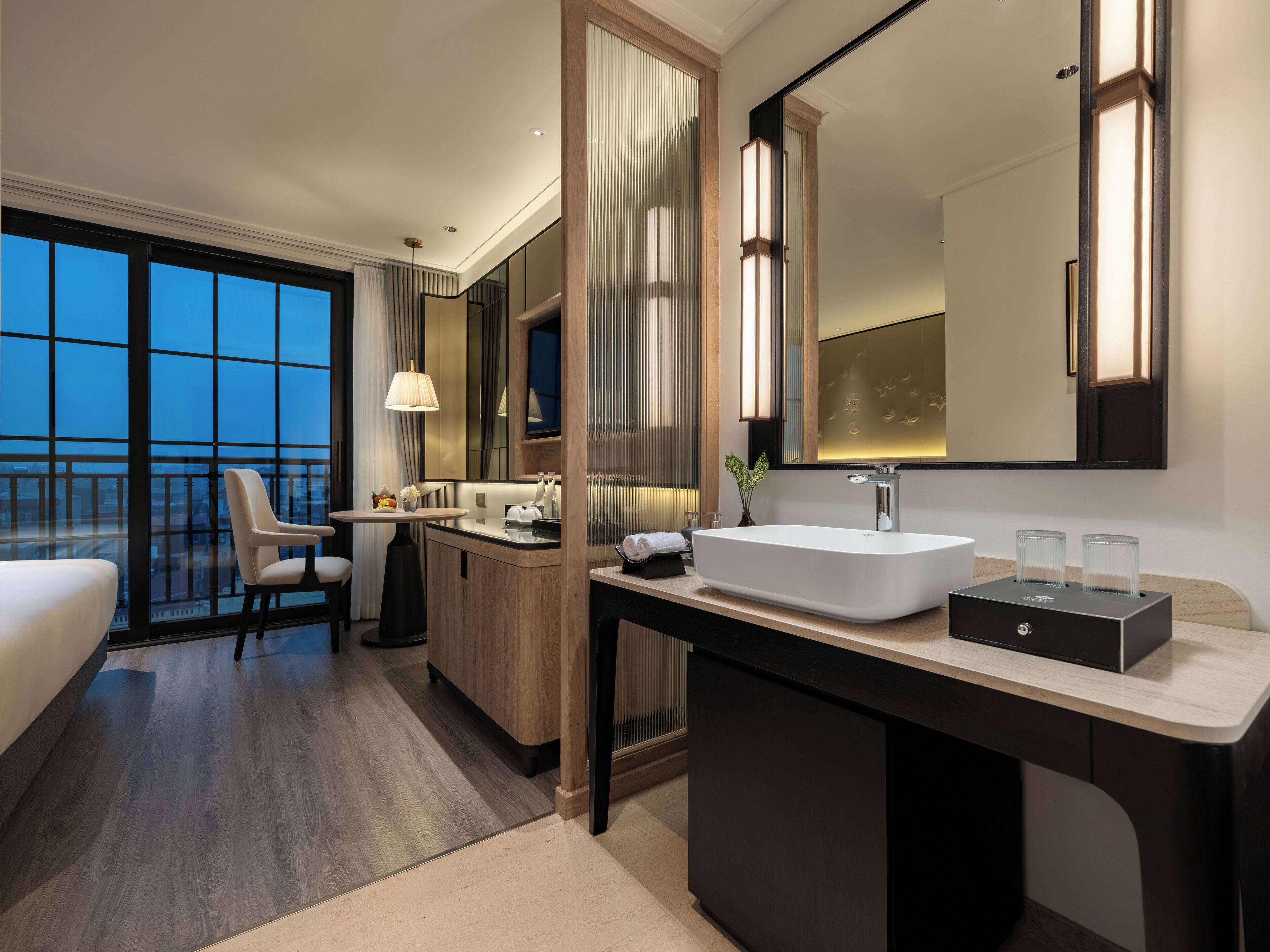 Une chambre d’hôtel moderne dotée d’une grande fenêtre, d’un lit, d’un bureau, d’une coiffeuse avec un miroir et d’une salle de bain avec un lavabo et des toilettes.