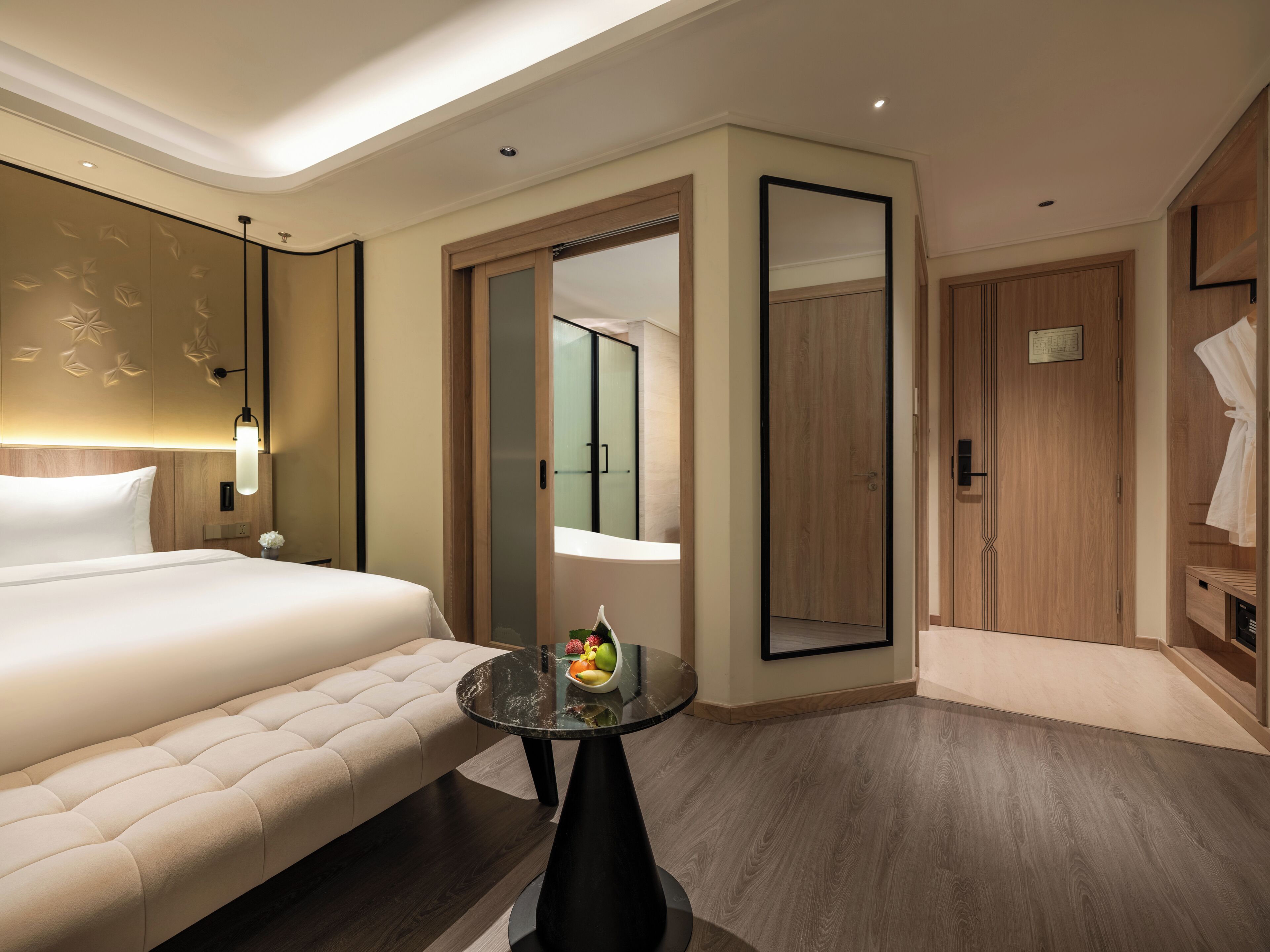 Una habitación de hotel con una cama grande, una mesa redonda con fruta, un espejo y un armario de madera.