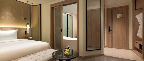 Una habitación de hotel con una cama grande, una mesa redonda con fruta, un espejo y un armario de madera.
