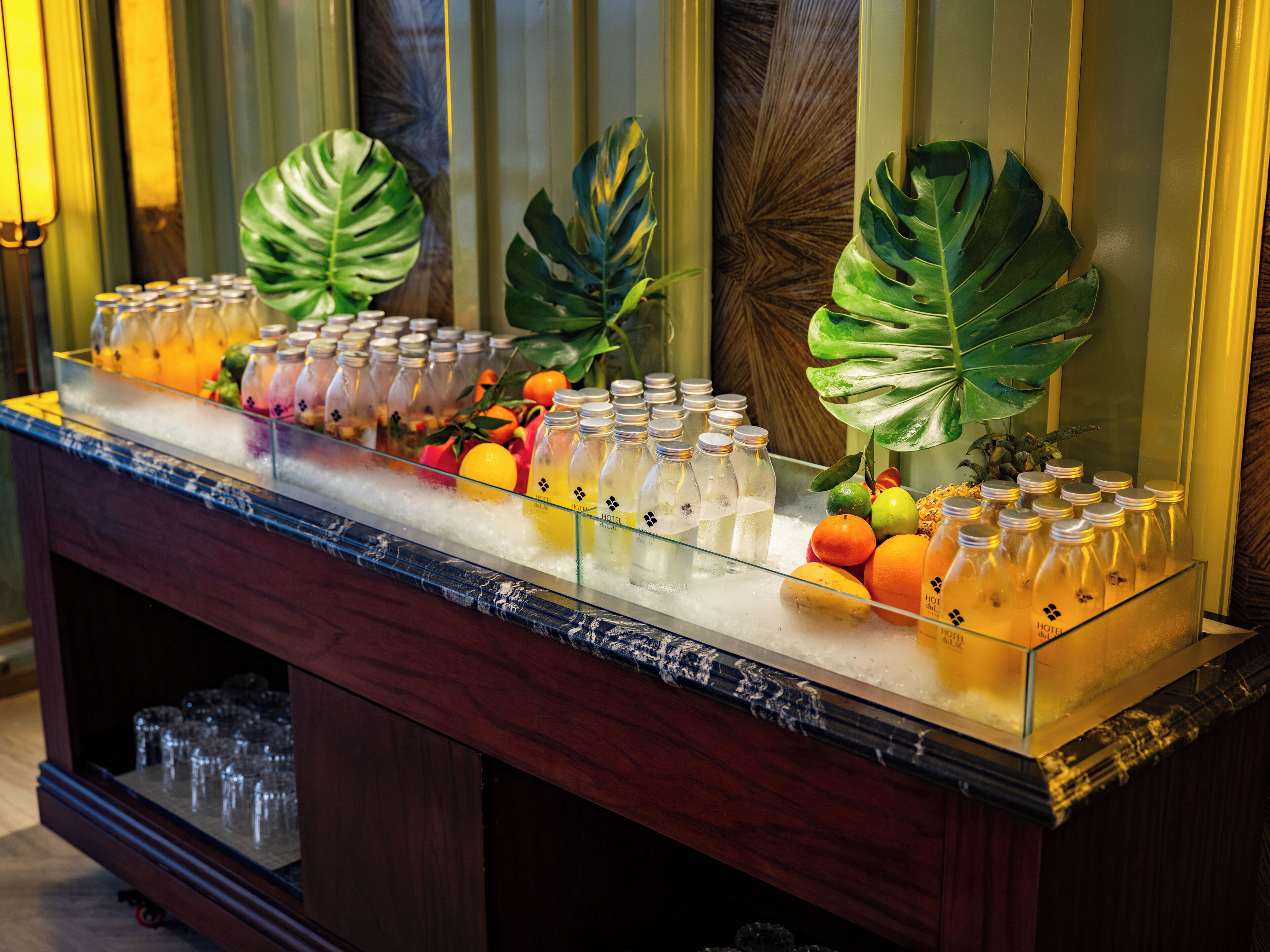 Un espace bar doté d’une vitrine réfrigérée où sont exposées des bouteilles de boissons et des fruits frais.
