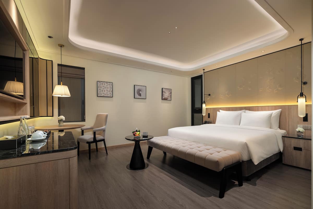 A modern hotel room with a large bed, a seating area, a small table, and a mirror.