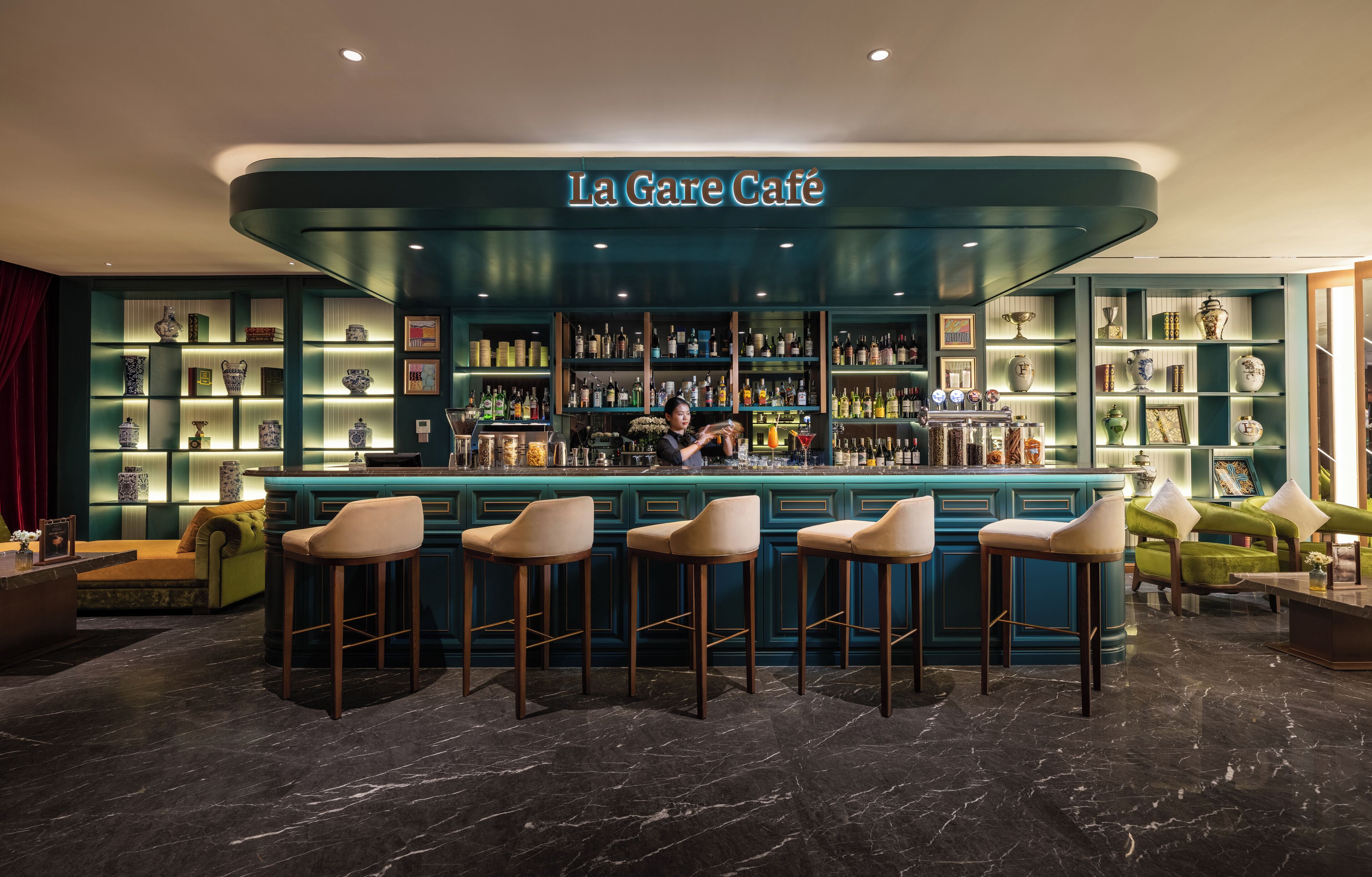 A bar area with a teal color scheme, bar stools, and shelves with various items.