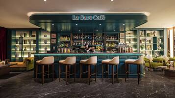 A bar area with a teal color scheme, bar stools, and shelves with various items.