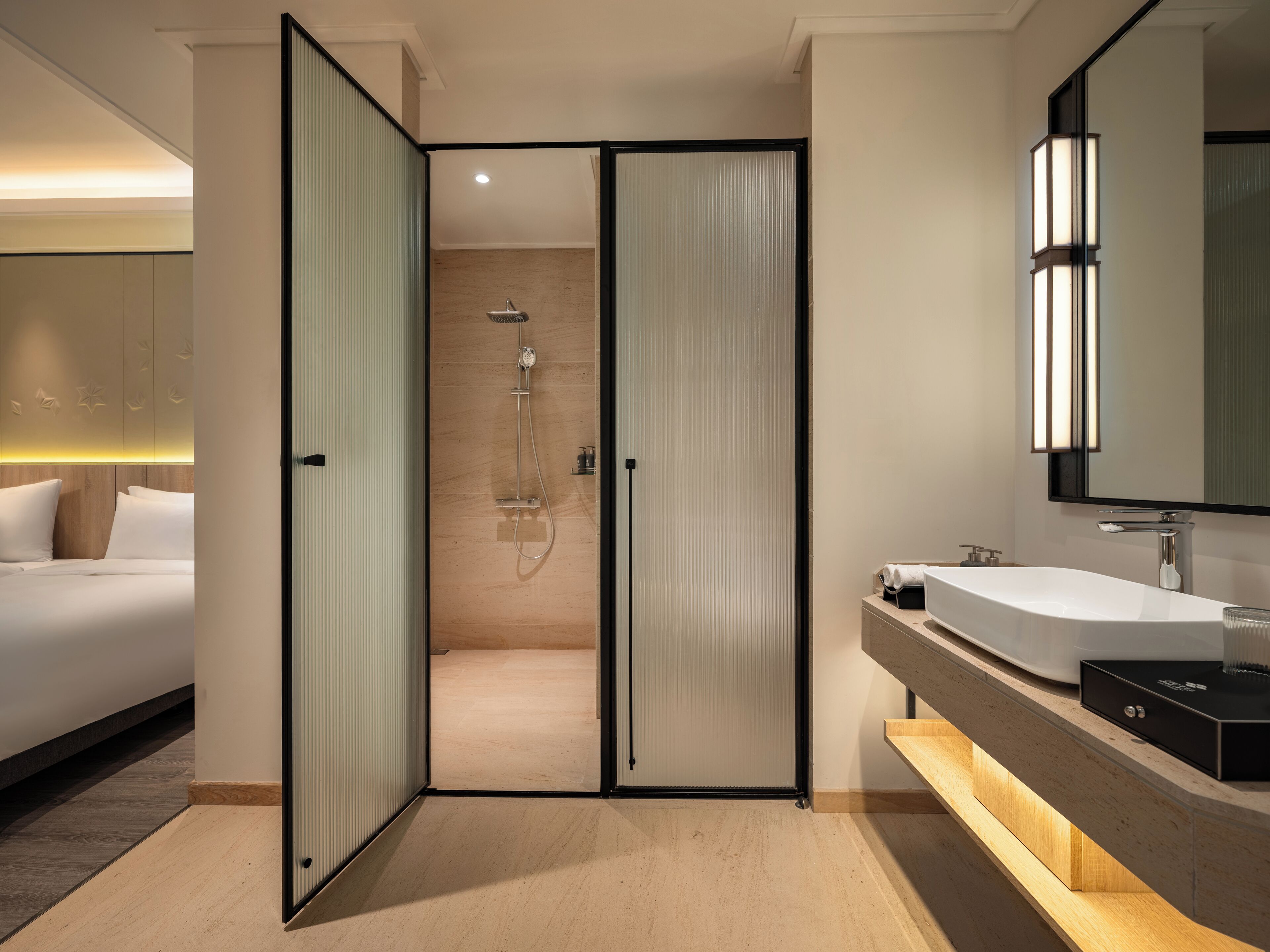 Une chambre d’hôtel moderne dotée d’une douche séparée, d’un grand miroir et d’une coiffeuse en bois.