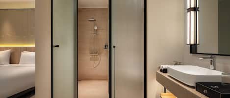 A modern hotel room with a separate shower area, a large mirror, and a wooden vanity.