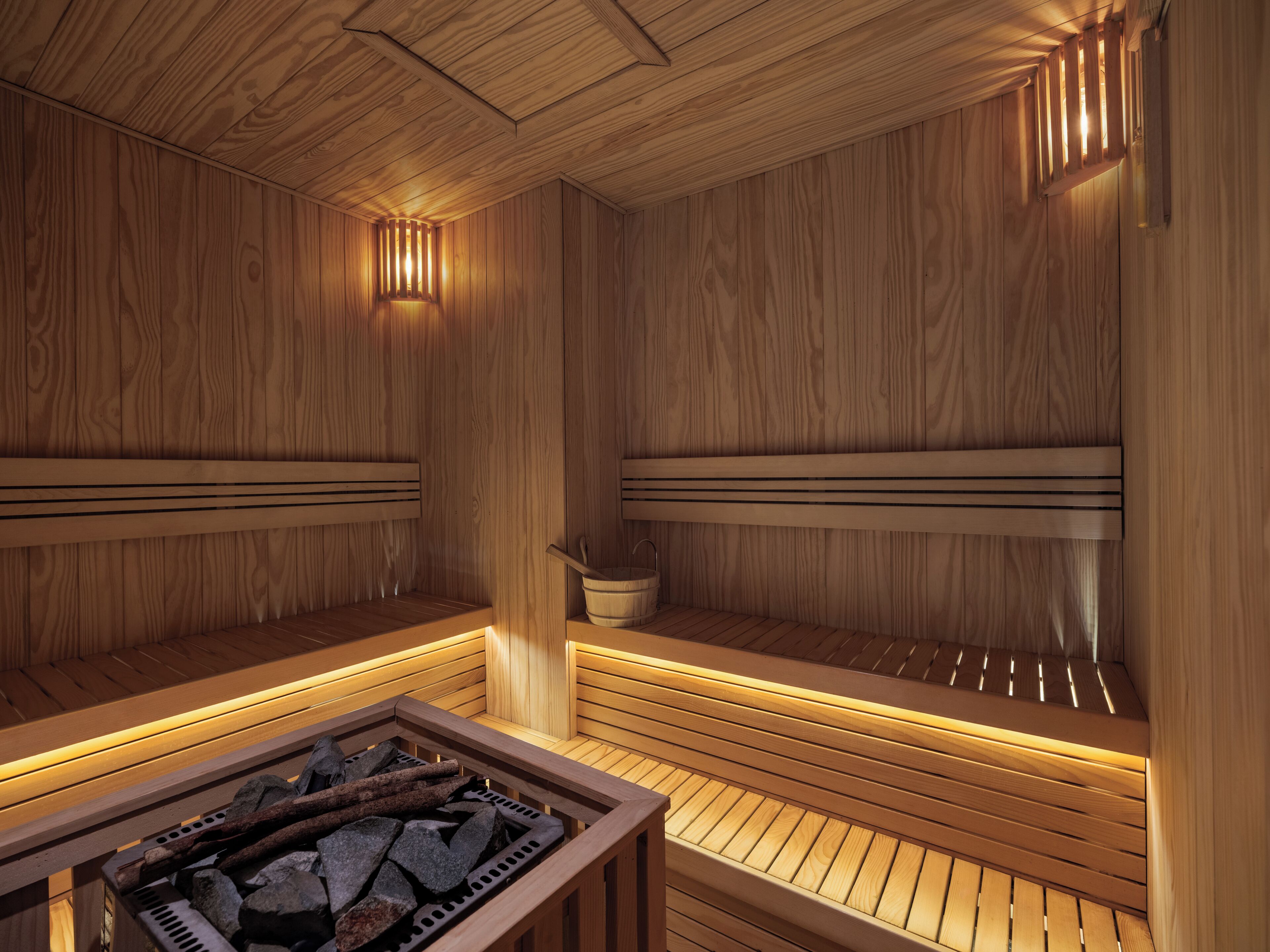 Un sauna aux murs et aux bancs en bois, un banc en pierre au premier plan et un seau accroché au mur.