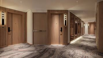 A hotel corridor with wooden doors, numbered room signs, and a patterned carpet.