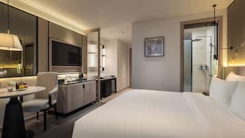 Une chambre d’hôtel moderne dotée d’un grand lit, d’un bureau avec une chaise, d’une petite table avec un vase et d’un espace douche.