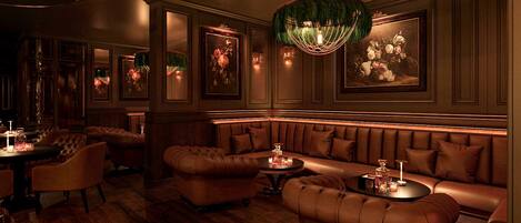 A luxurious lounge with leather seating, a chandelier, and framed floral artwork.