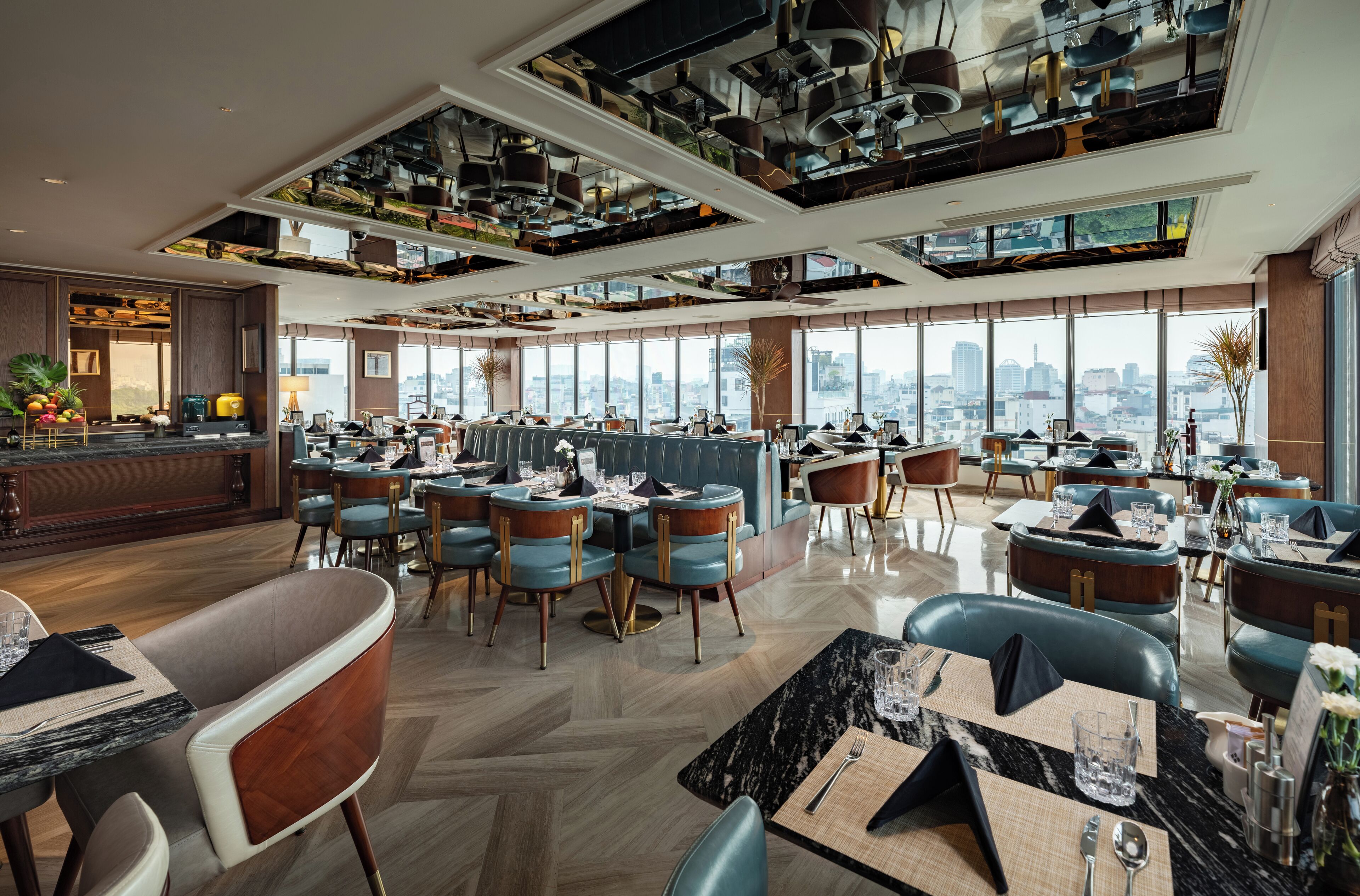 A spacious restaurant with multiple dining areas, large windows offering city views, and a modern ceiling design with hanging lights.