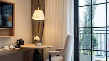 A hotel room with a round table, a chair, a lamp, a coffee maker, and a TV on the wall.