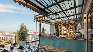 Un bar en la azotea con vistas a la ciudad, un barman y un área de descanso con mesas y sillas.