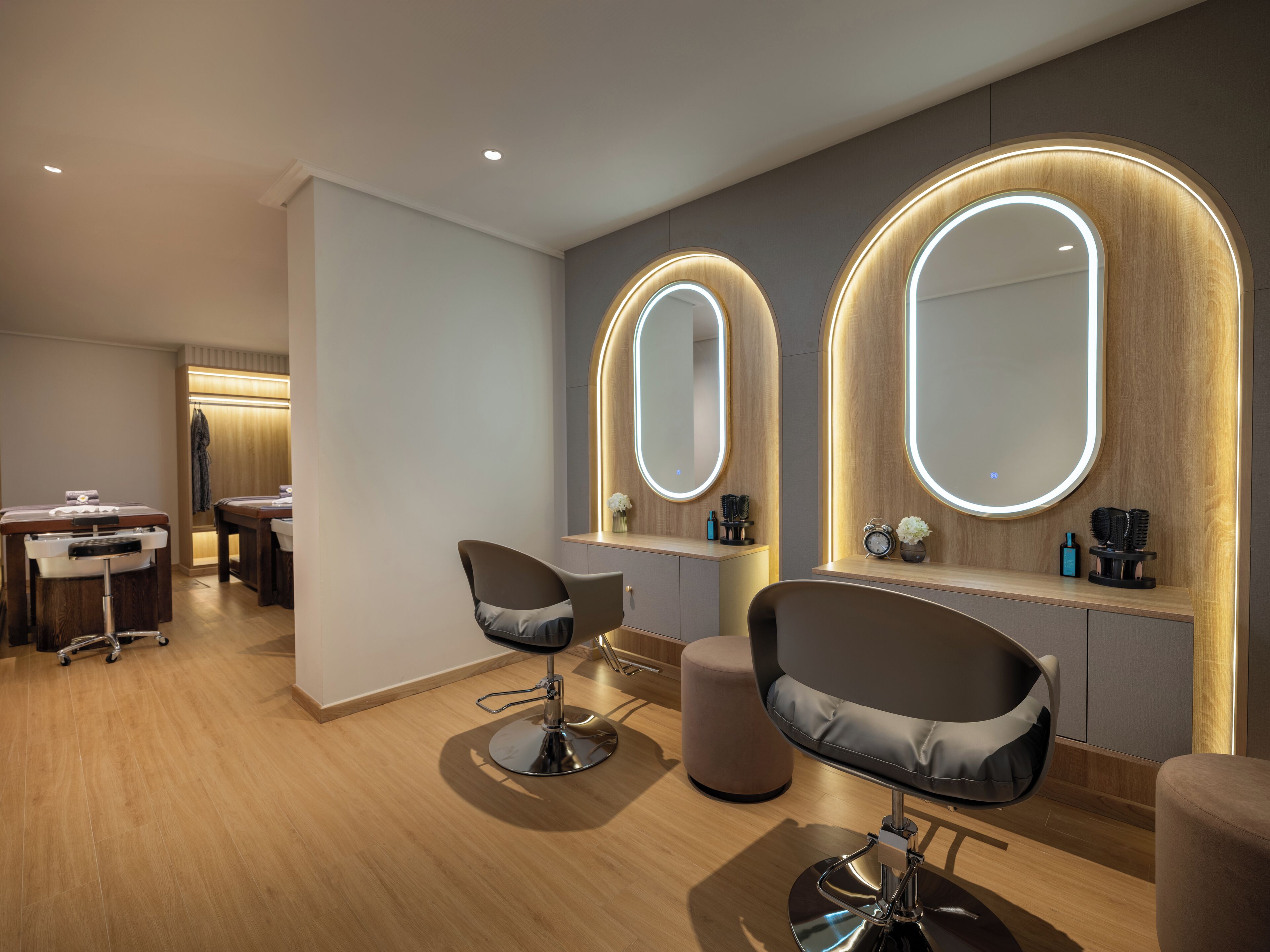 Un salón moderno con dos espejos grandes, una estación de lavado de cabello y un área de asientos con sillones acolchados.