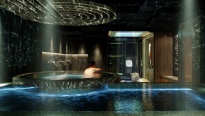 Un área de spa con un jacuzzi grande, paredes de mármol y un diseño de techo moderno.