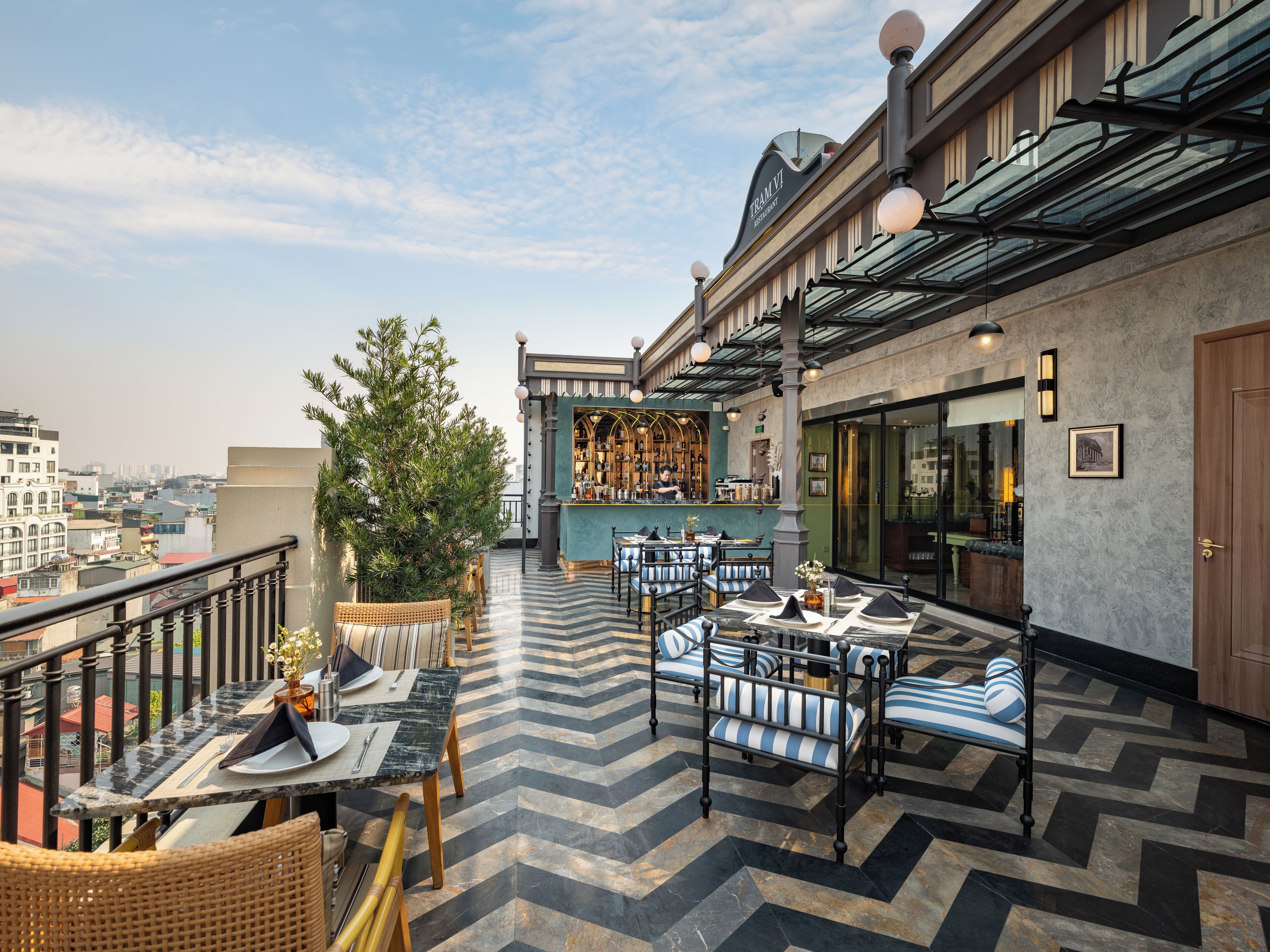 A rooftop terrace with outdoor seating, a bar, and a view of the city.