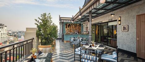 A rooftop terrace with outdoor seating, a bar, and a view of the city.