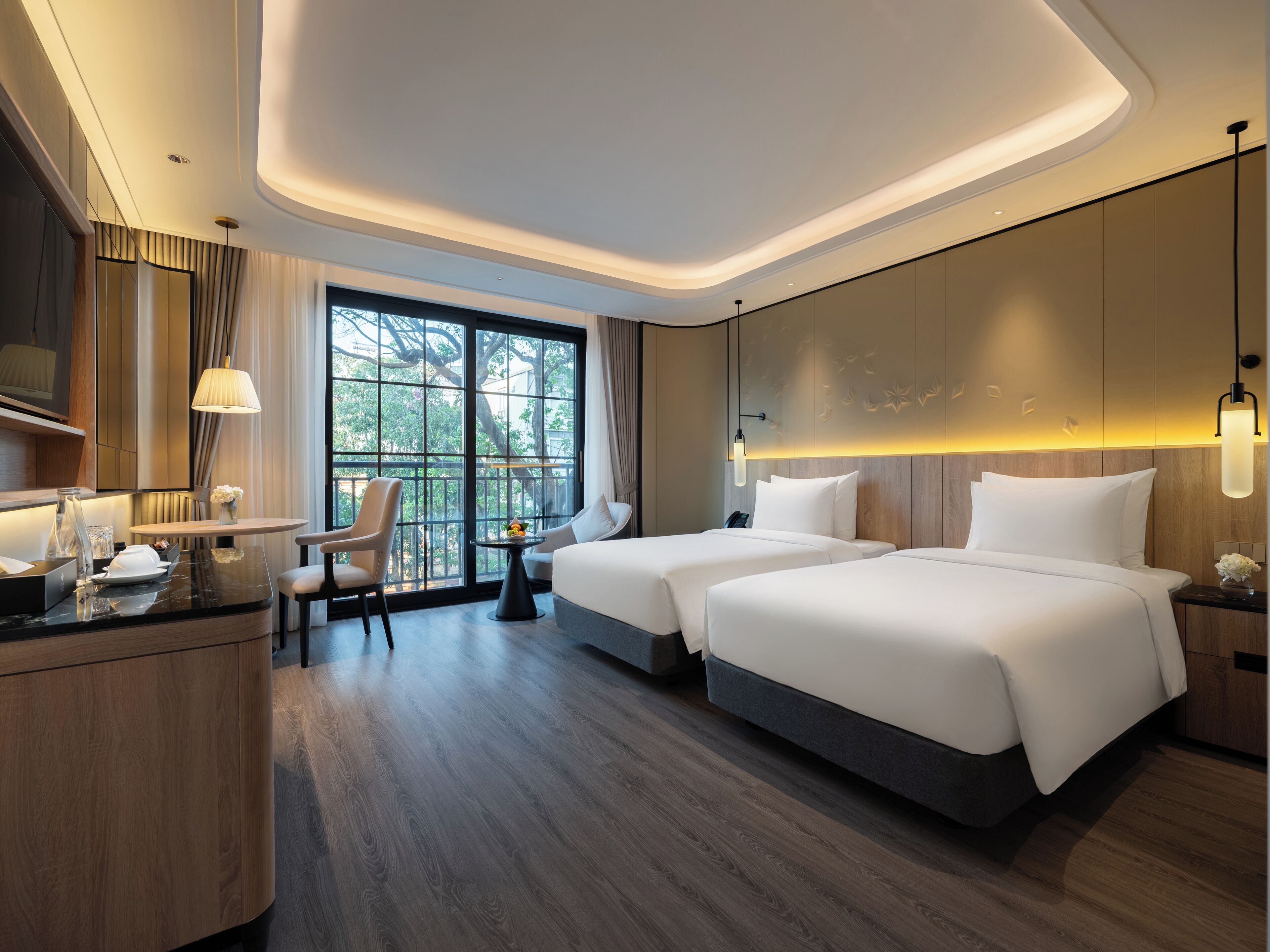Une chambre d’hôtel moderne avec deux lits, un bureau et une grande fenêtre donnant sur la verdure.
