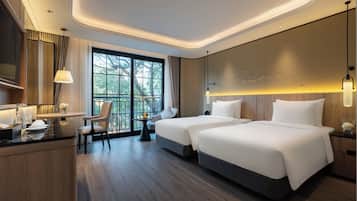 Une chambre d’hôtel moderne avec deux lits, un bureau et une grande fenêtre donnant sur la verdure.