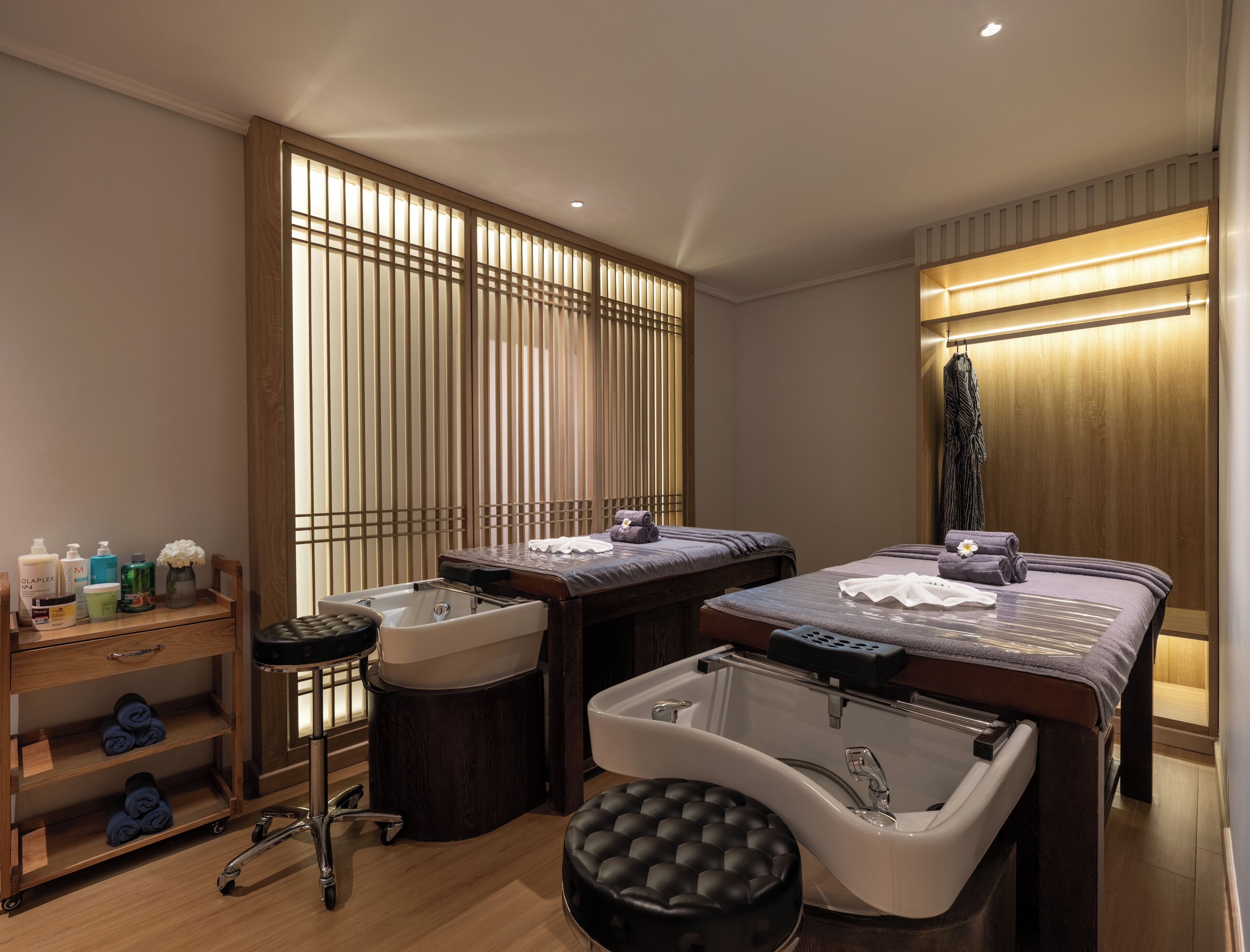 Un cuarto de spa con dos camillas de masaje, una bañera grande y un estante de madera con artículos de aseo.