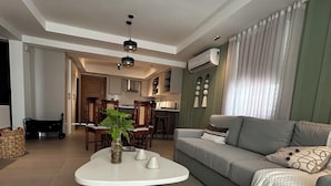 Un salon moderne avec un canapé gris, une table basse ronde et un coin repas comprenant une table et des chaises en bois.