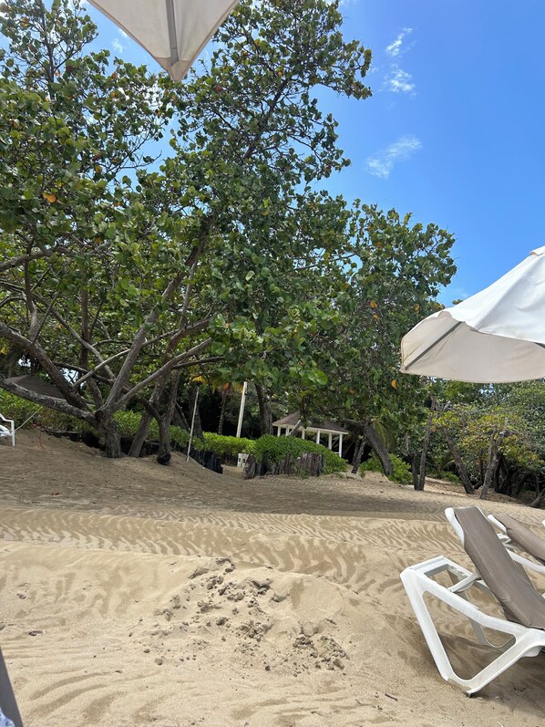 A sandy beach area with a white umbrella and a lounge chair.