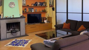Un salon avec une cheminée, un canapé, un téléviseur et un luminaire décoratif au plafond.