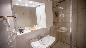 A bathroom with a white sink, a mirror, a hairdryer, and a shower area. - Hôtel la Picholine en Provence (Nyons)