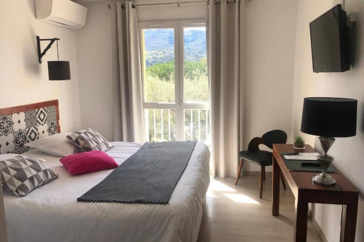 A bedroom with a bed, a desk, a chair, a TV, and a window with curtains.