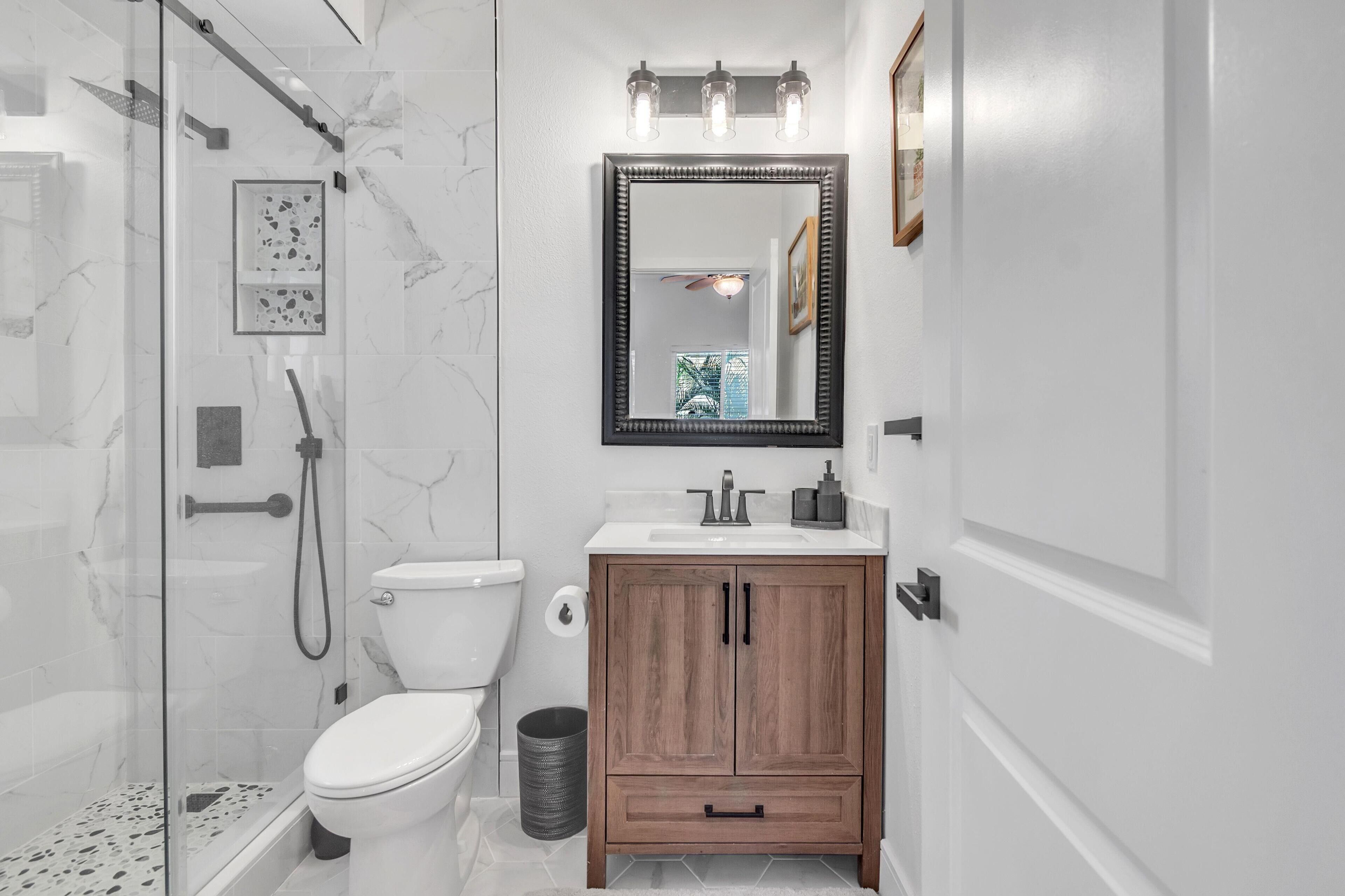 A modern bathroom with a glass-enclosed shower, a toilet, a vanity with a mirror, and a wooden cabinet.